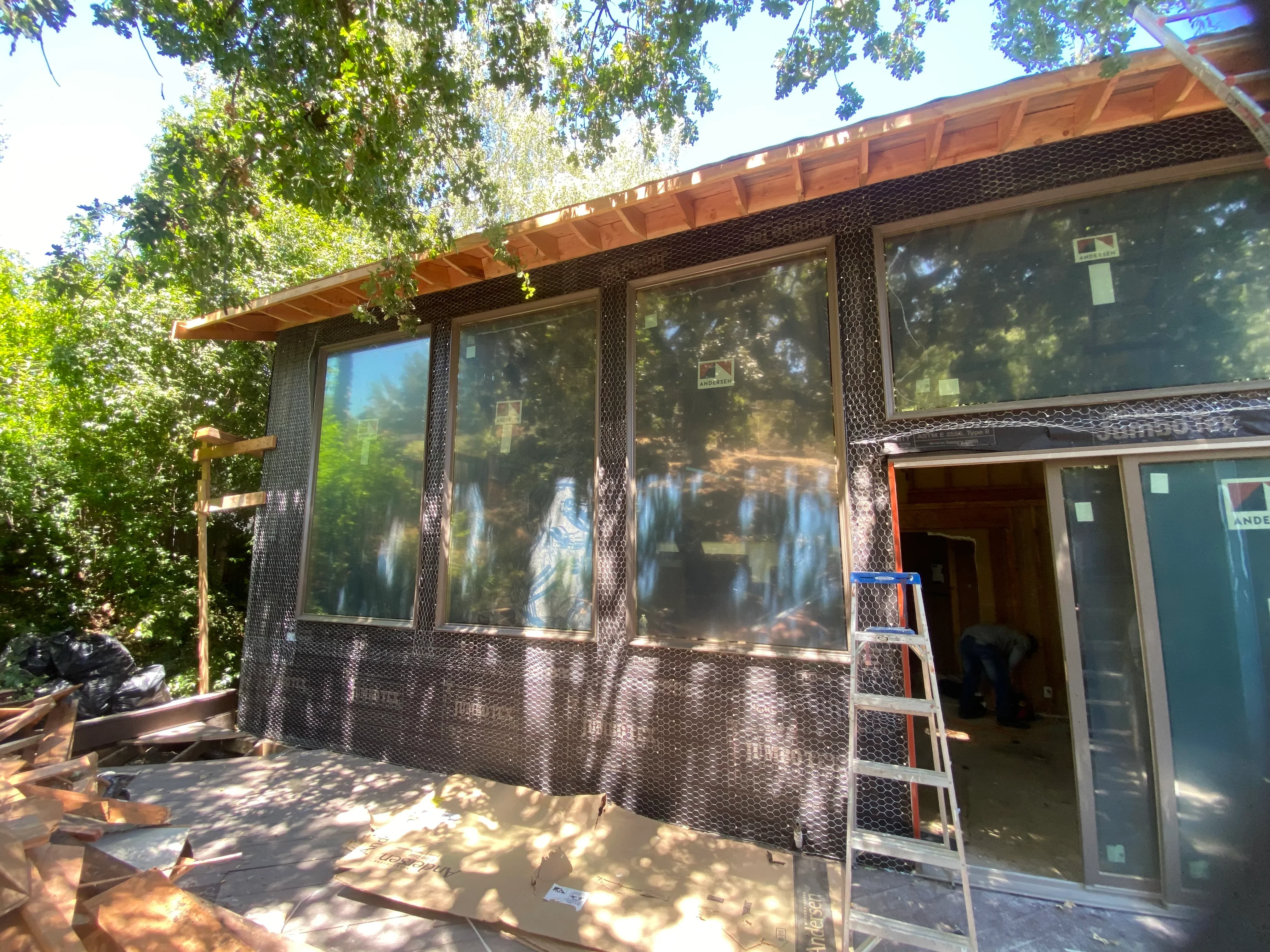 Wood pergola with metal screening over large windows and glass doors in shaded backyard