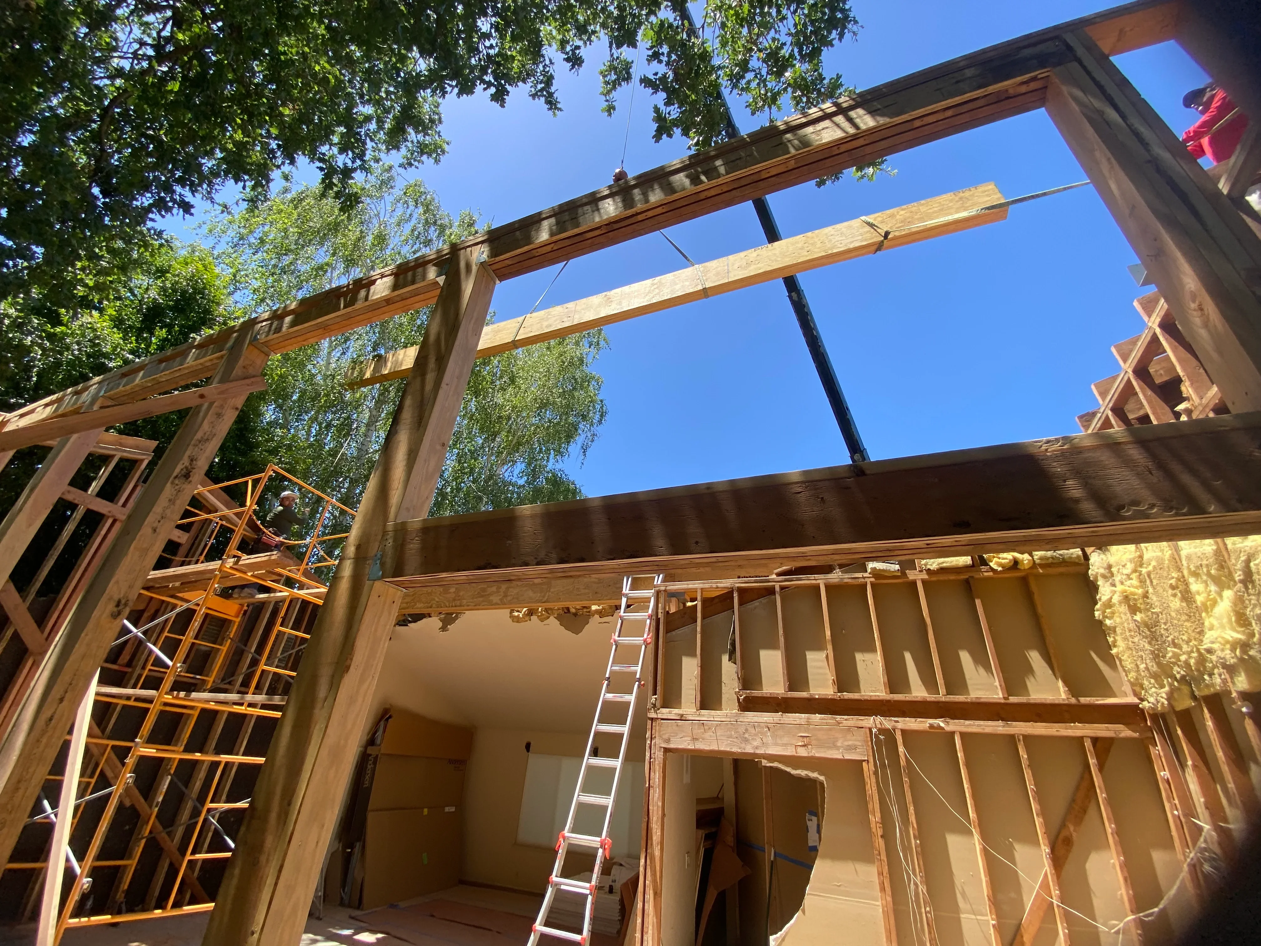 Residential addition framing with exposed beams, steel supports, and drywall installation in progress