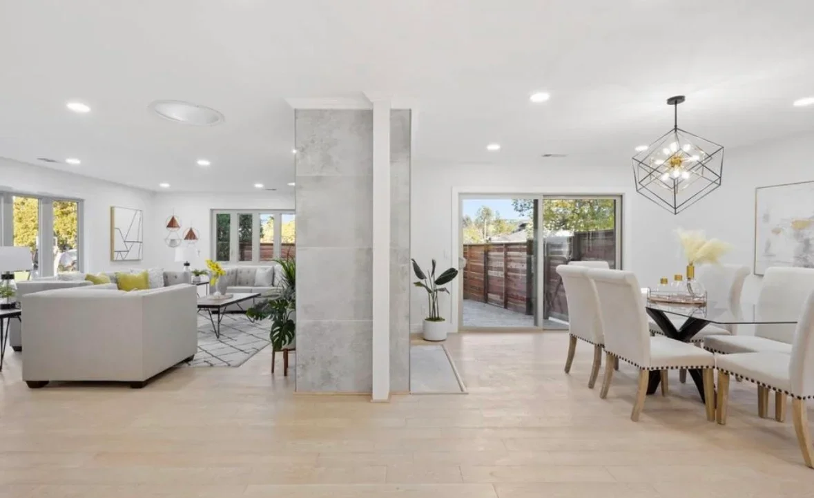 Modern open-concept living and dining area with light wood floors, white walls, and glass doors to patio