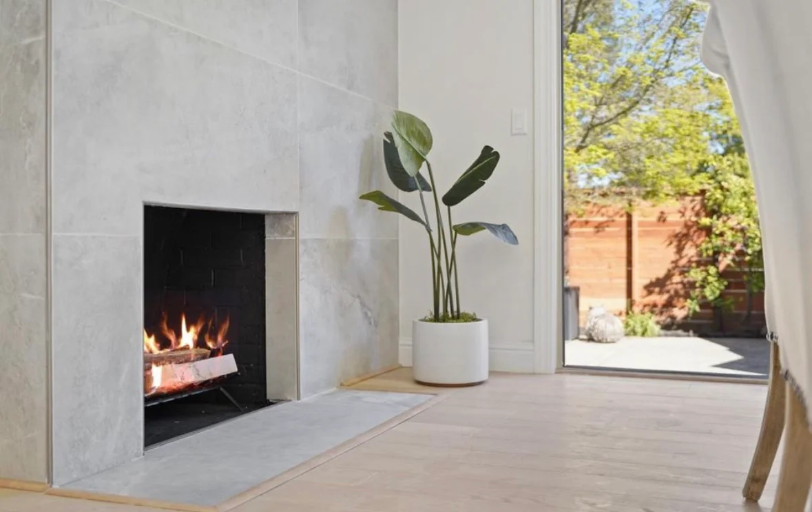 Modern fireplace with gray tile surround, light wood flooring, and glass patio doors
