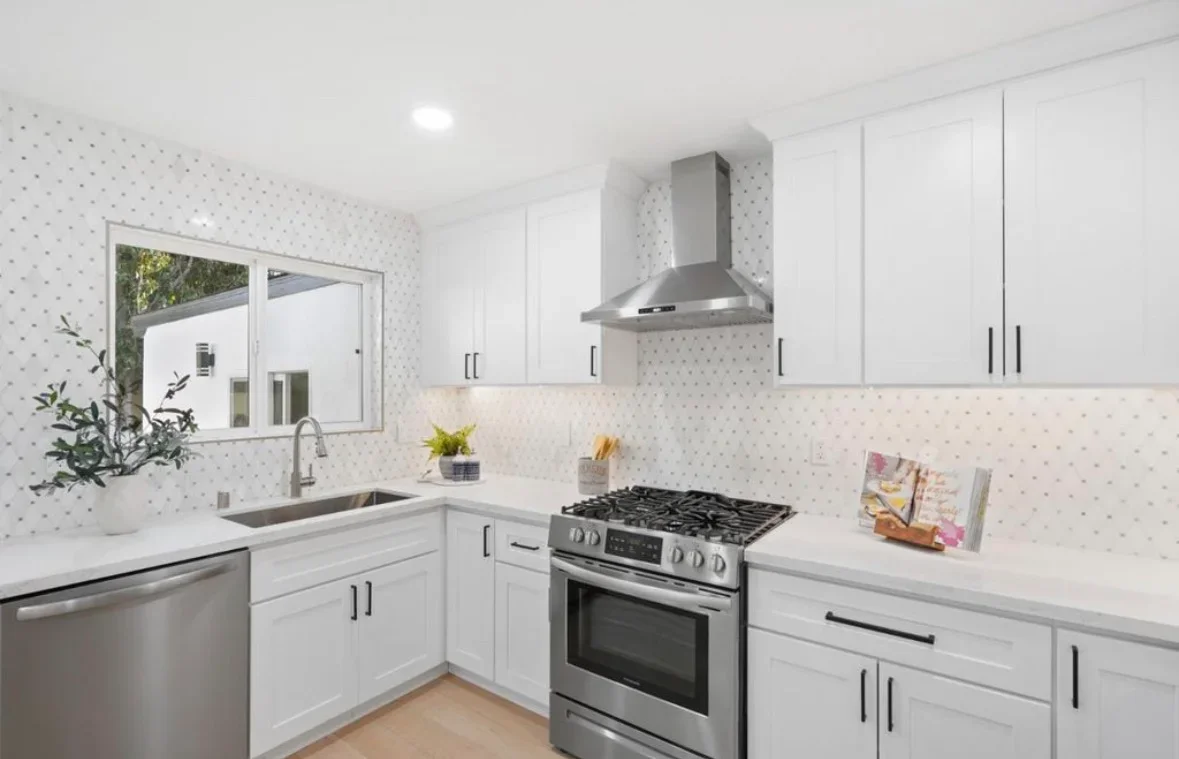Modern white kitchen with gas range, white cabinetry, quartz counters, and geometric tile backsplash