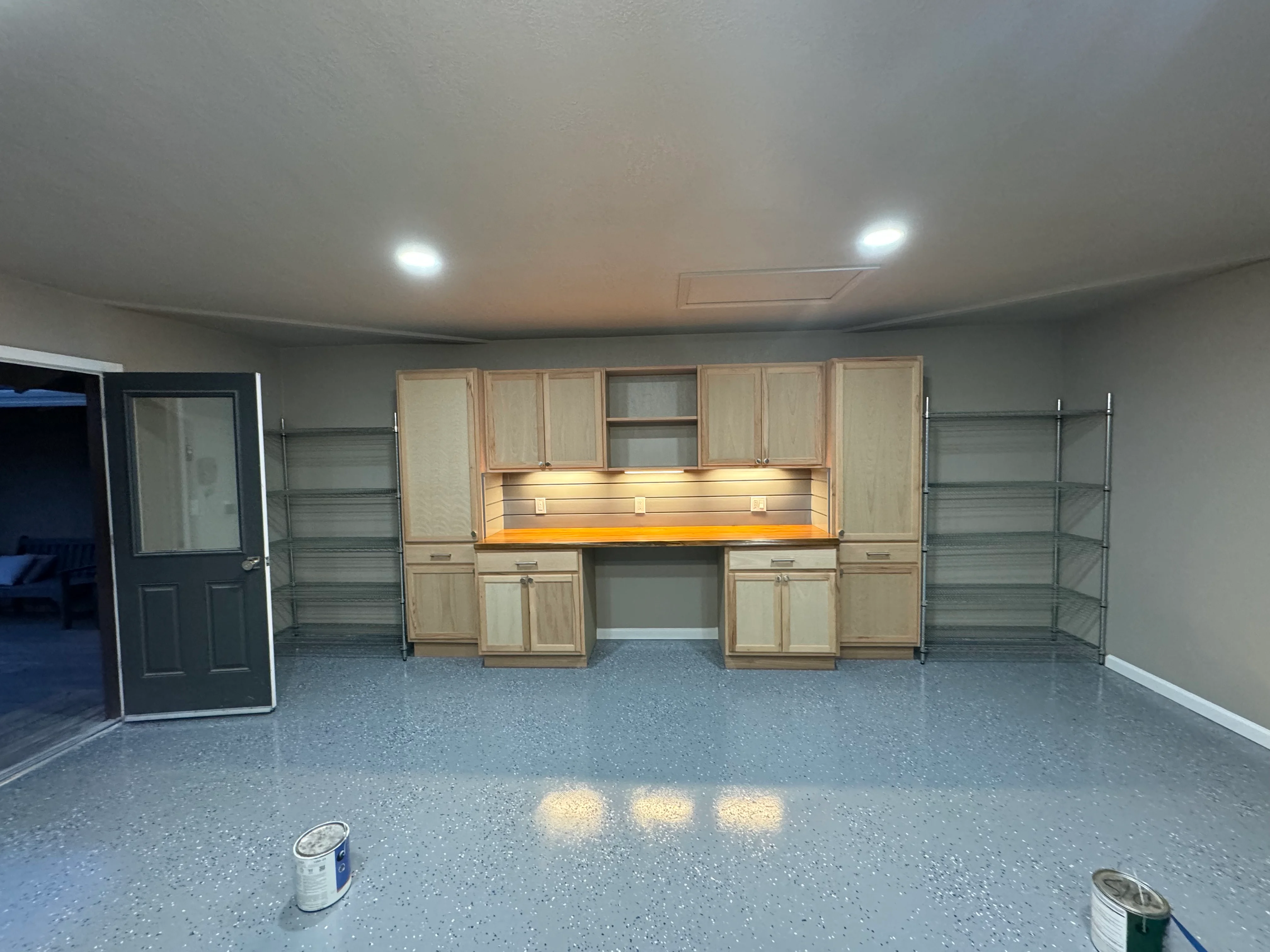 Garage interior with wooden cabinetry, metal shelving, LED lighting, and epoxy concrete floor