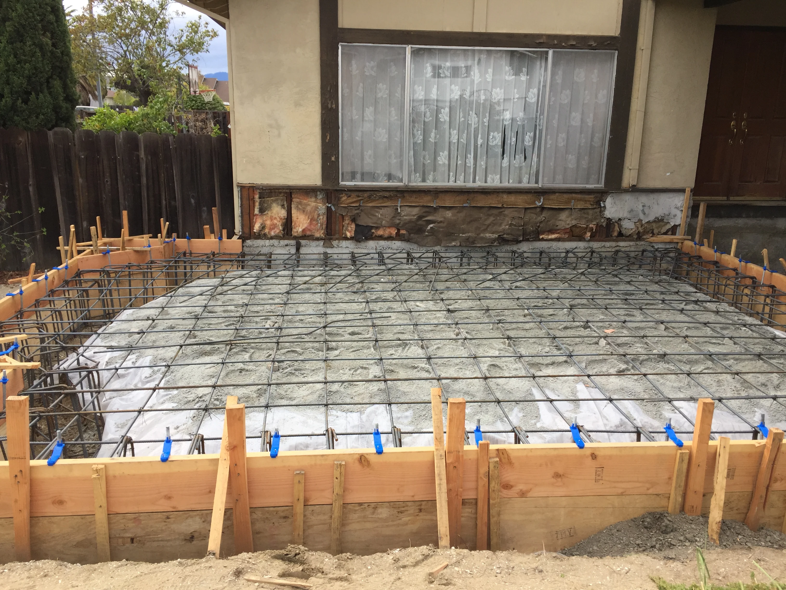 Concrete foundation with steel rebar grid, wooden forms, and blue bracing clamps