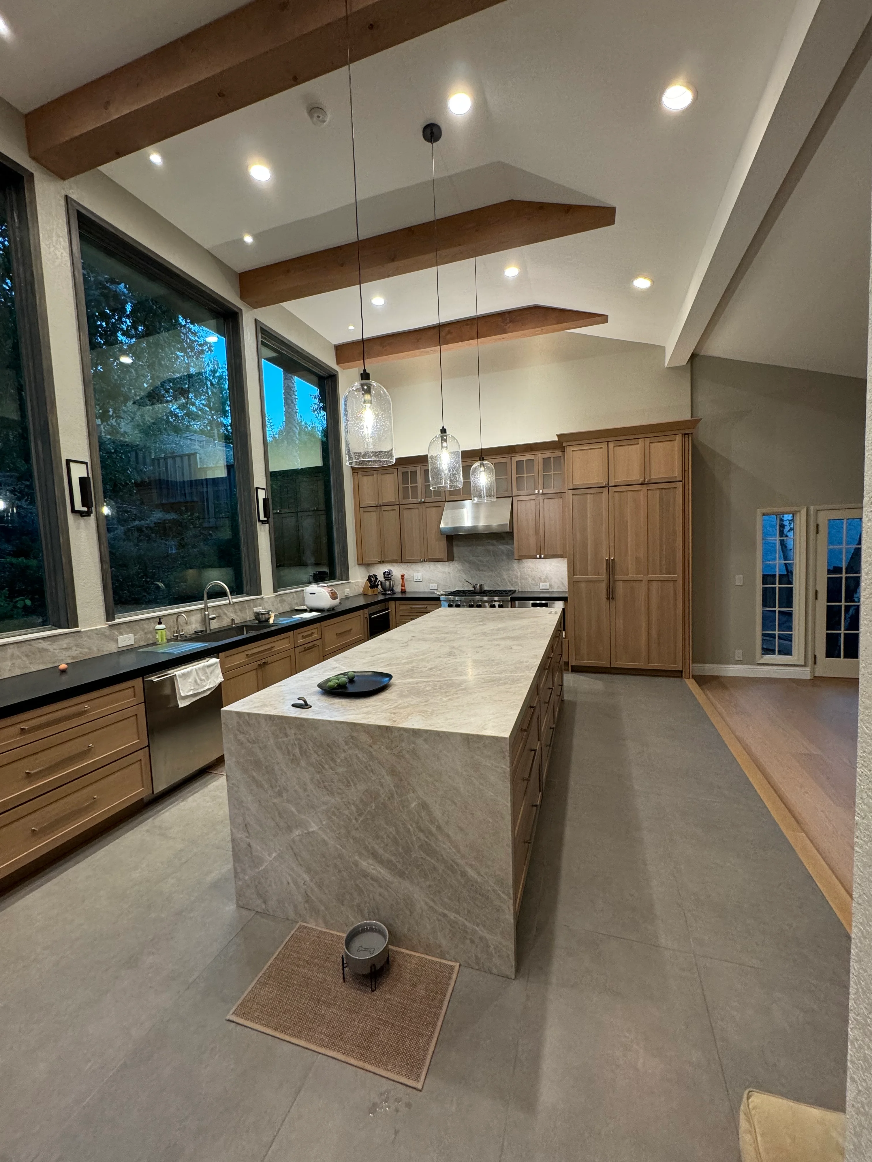 Modern kitchen with wood cabinetry, marble island, pendant lights, and vaulted ceiling with exposed beams